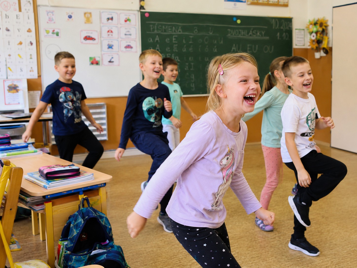 Děti při radostné pohybové aktivitě ve třídě základní školy.