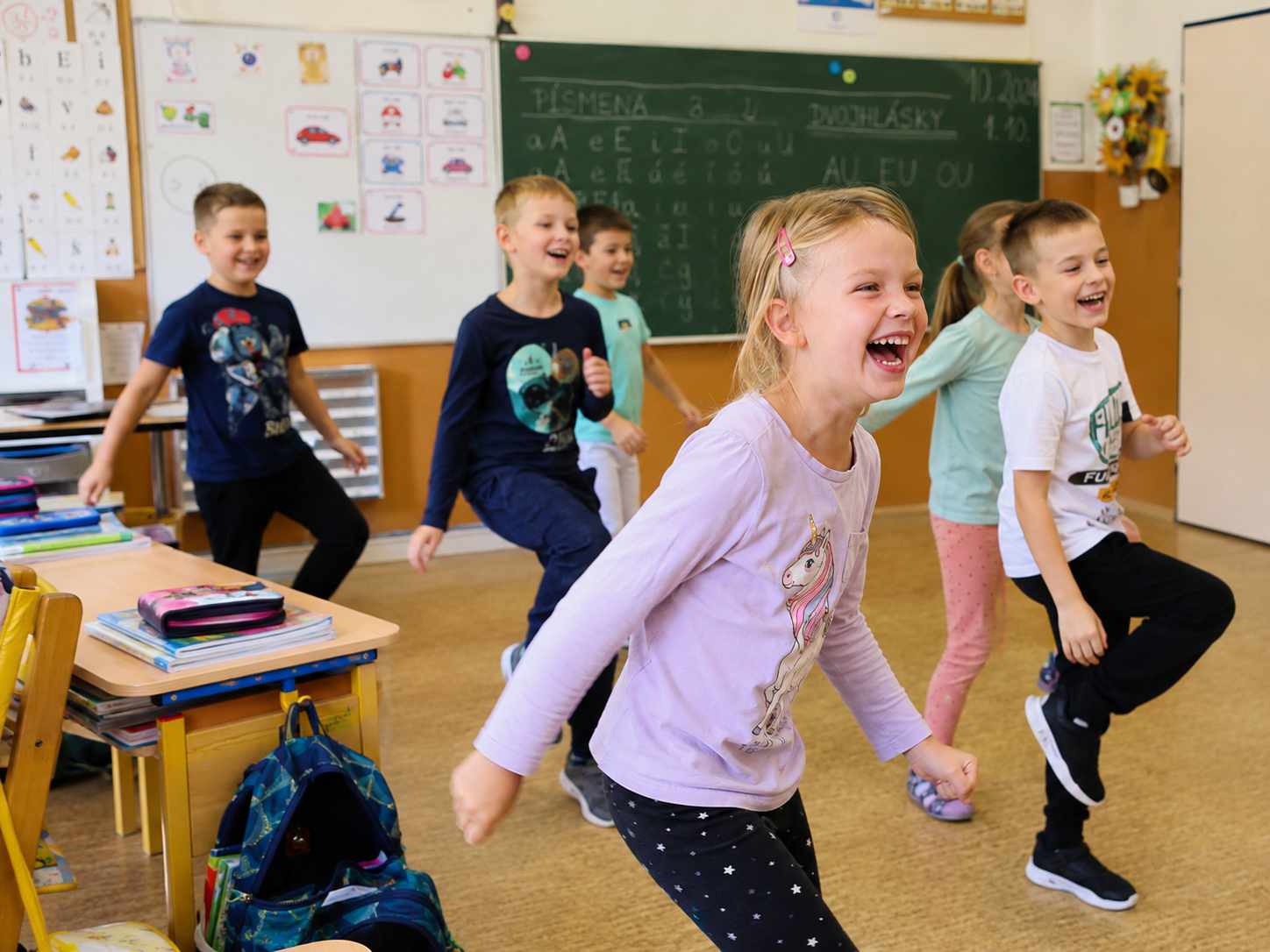 Děti při radostné pohybové aktivitě ve třídě základní školy.